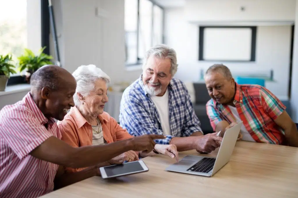 A group of four seniors look at a laptop computer and a tablet.