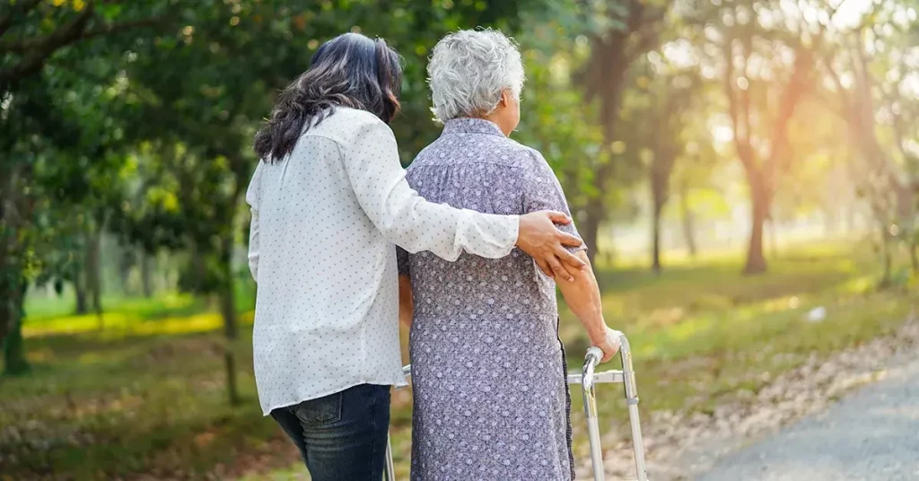 An elderly woman walking down an outdoor path with a companion.