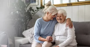 An elderly woman sitting on a couch with her adult daughter.